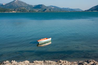 Dağların önündeki sakin, berrak suda tek başına duran küçük turuncu-beyaz bir kayık
